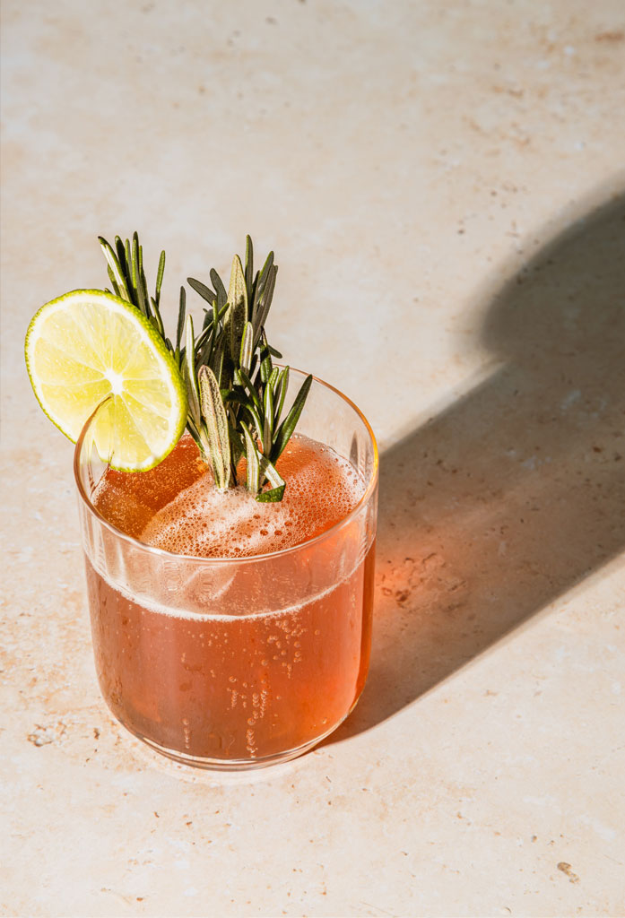 Pink cocktail drink with a lime and rosemary garnish